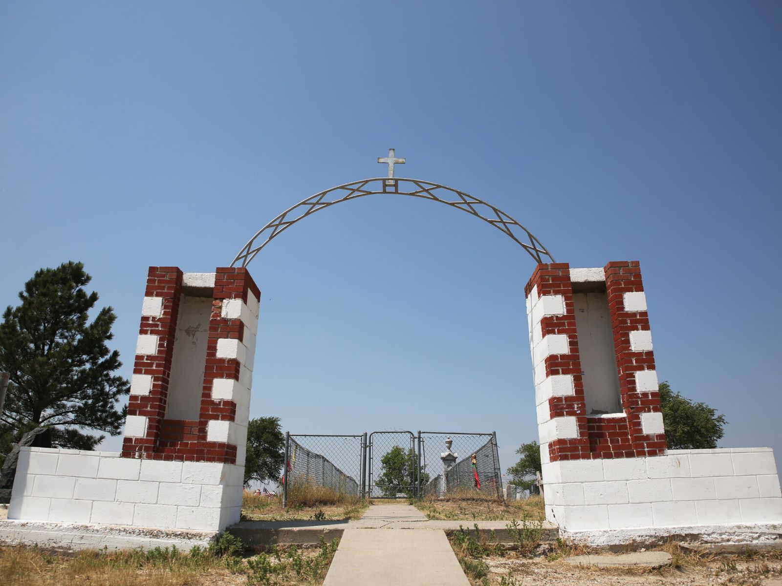 An arch topped with a cross marks the entrance to the Wounded Knee Memorial and cemetery on the Pine Ridge Reservation in South Dakota on June 30, 2024. (South Dakota Searchlight/Makenzie Huber)
