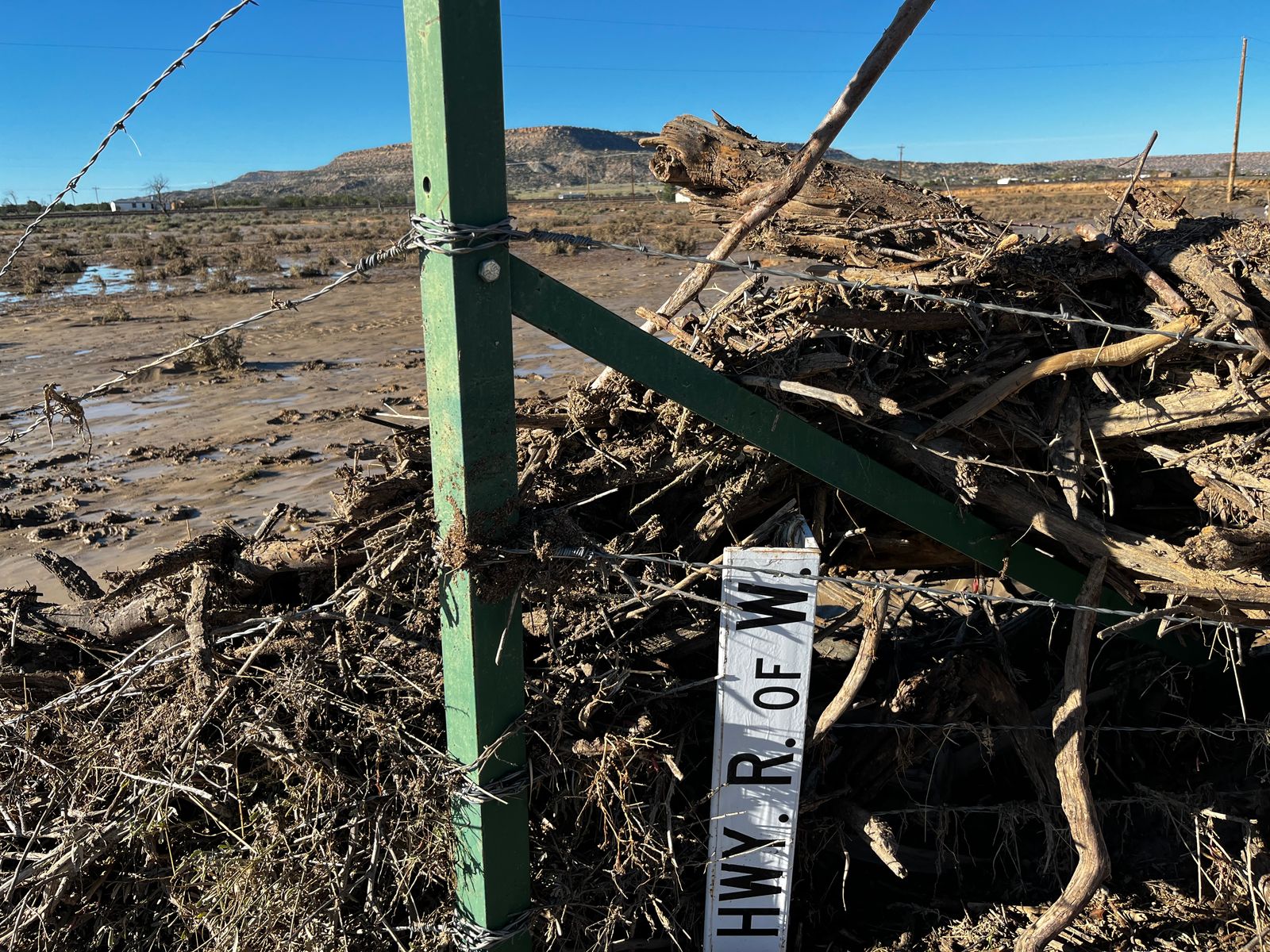 A highway sign sits in debris from flooding that occurred when rain over the weekend breached flood control in the Rio San Jose in Laguna Pueblo.