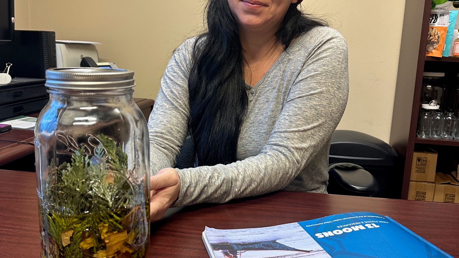 Beth Willup, the Swinomish Tribe’s environmental health program coordinator, sits in her office with a jar of preserved medicinal plants on her desk, January 2025. Making healing salves from medicinal plants is an activity during the Moon of the Salmonberry.