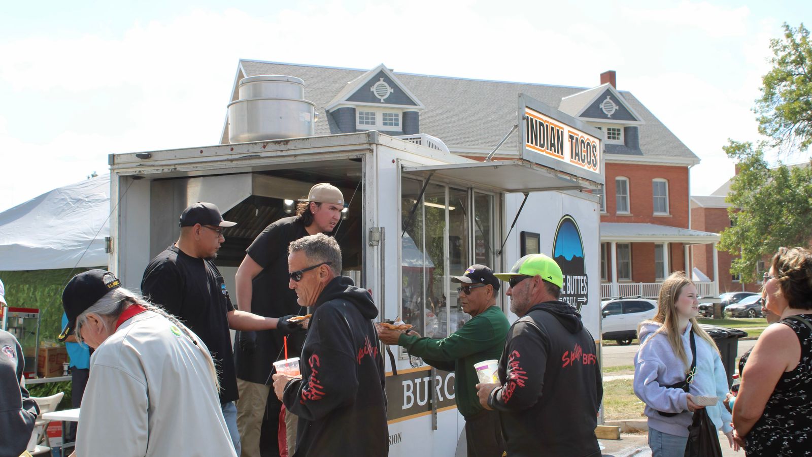 Blue Buttes Grill cook Jordan Davis (in tan hat) hands frybread to a customer while other powwow attendees wait for their food, Bismarck, North Dakota, Saturday, Sept. 6, 2025.  (Buffalo’s Fire Photo/Gabrielle Nelson)
