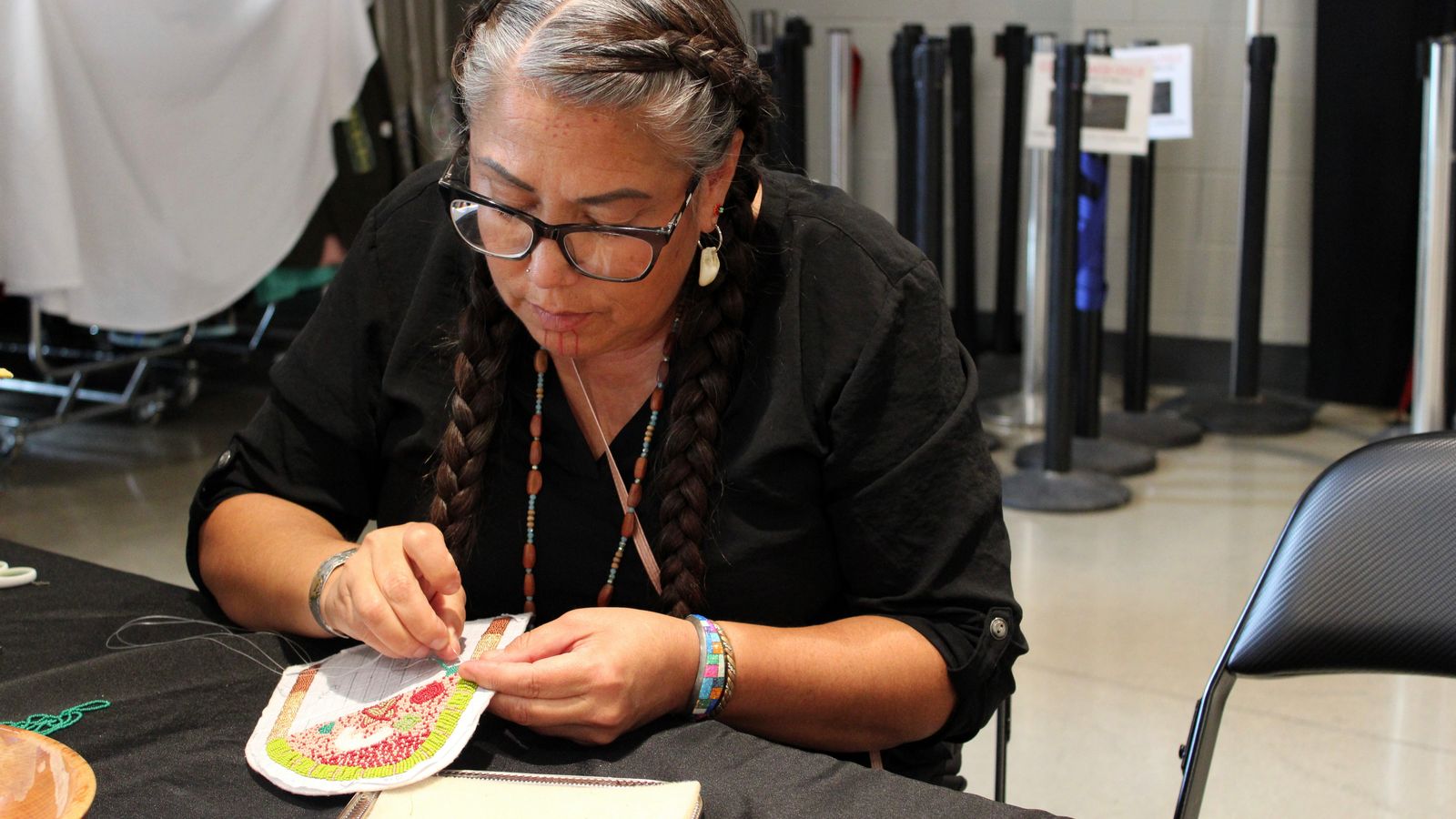 Kelly Hosie beads a piece of regalia at the Four Bears Casino. She sold her beadwork and baked items at a booth during the alterNATIVE Medicine Symposium and attended sessions to learn more about medical marijuana, July 29, 2025. (Photo credit: Gabrielle Nelson)
