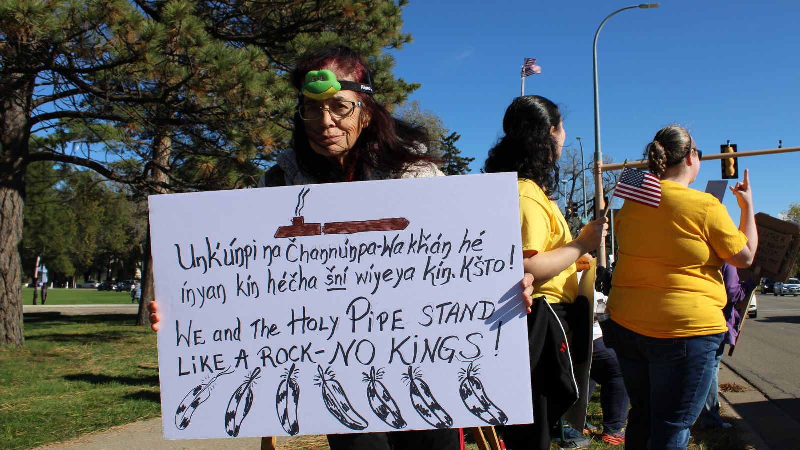 At the “No Kings” rally, Carel Two-Eagle (Lakota), a Pipe Carrier and Sundancer, holds a sign that reads in Lakota and English, “We and the Holy Pipe stand like a rock — NO KINGS!” Bismarck, North Dakota, Saturday, Oct. 18, 2025. (Buffalo’s Fire/Gabrielle Nelson)