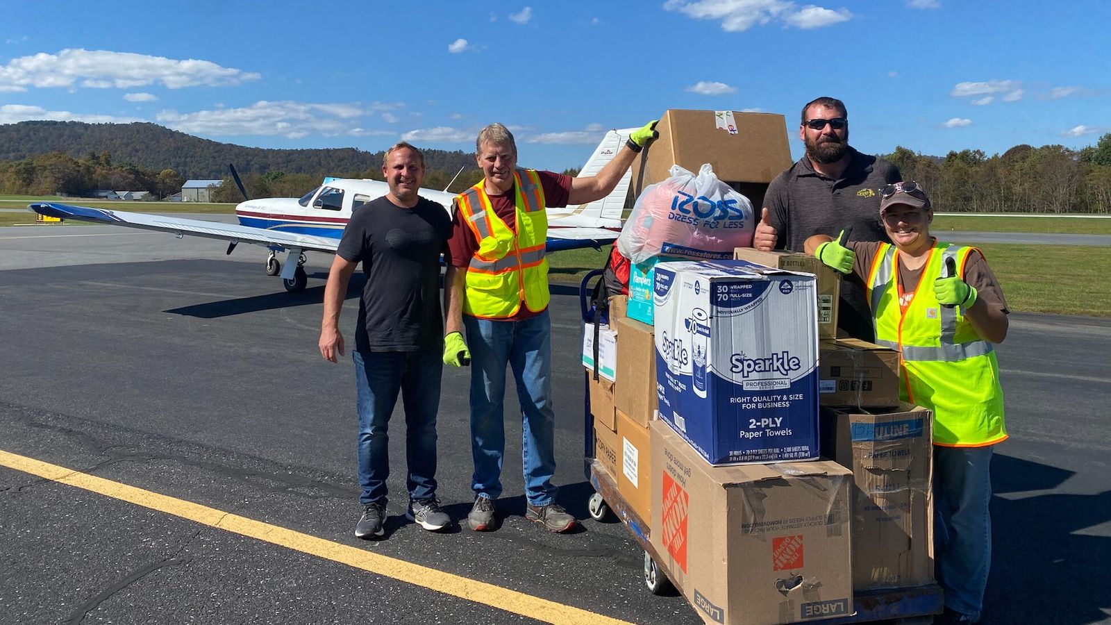 Casey Veil (left, black shirt) and Treven Iverson (right, sunglasses) of Jamestown pose with volunteers and the supplies they flew into a distribution point in Jefferson, N.C. on Oct. 5. Contributed by Veil. 