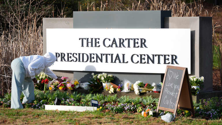 Christine Mason, of Atlanta, places flowers at the entrance to The Jimmy Carter Presidential Center in Atlanta, Georgia, on Monday, Dec. 30, 2024. Formr President Jimmy Carter died Sunday at his home in Plains, Georgia, at the age of 100. (AP Photo/John Bazemore )